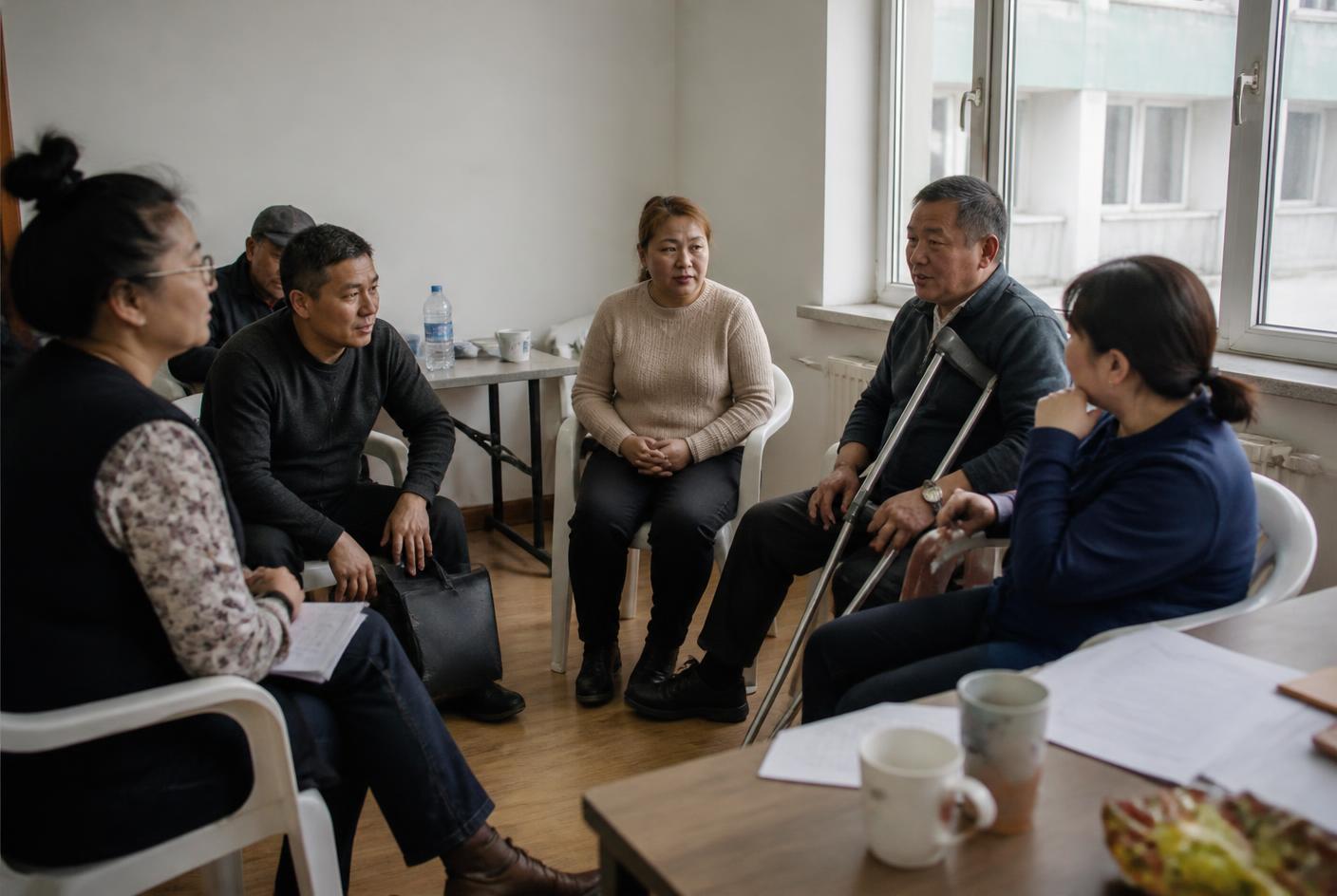 Residents and staff sitting in a circle of plastic chairs during a community meeting in a modest room in Ulaanbaatar.